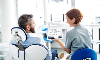 Dentist and patient smiling as they discuss X-ray on tablet