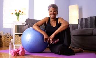 A middle-aged woman sitting on the floor doing her exercises while smiling after receiving implant dentures