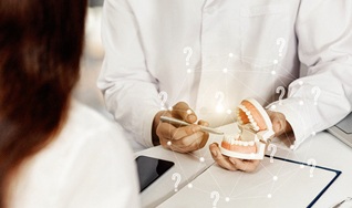 A dentist uses a mouth mold to explain the process of receiving dental implants to a patient