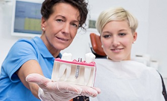 Implant dentist holding model of dental implants in front of a patient