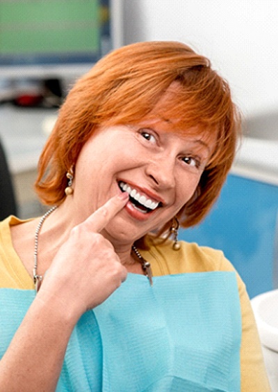 An older woman with red hair points to her teeth that received same-day crowns in Westminster