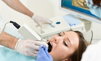 A dentist uses an intraoral scanner on a female patient’s smile