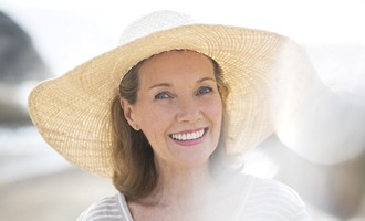 An older woman wearing a large hat smiles after receiving her same-day crowns