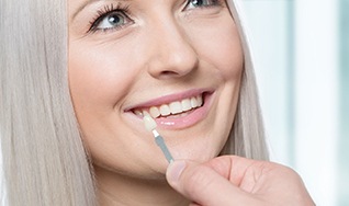 A young woman shows her teeth while a dentist uses a shade guide to determine the color of her veneers