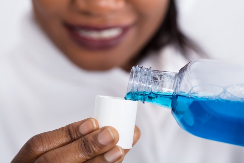 a woman pouring mouthwash into a cup to rinse out her mouth 