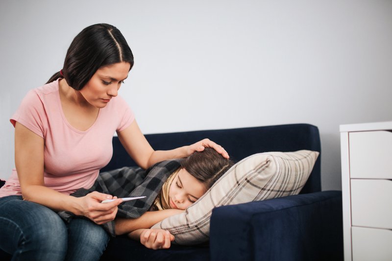 a woman sitting on a couch checking her daughter’s temperature 