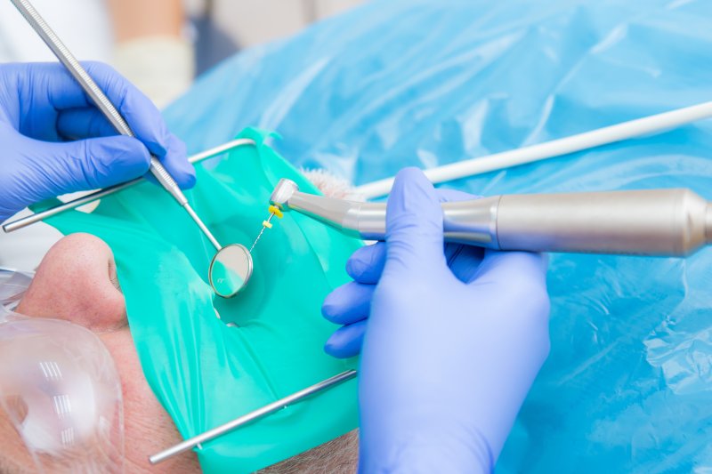 a dentist using a dental dam and preparing to perform a root canal on a patient