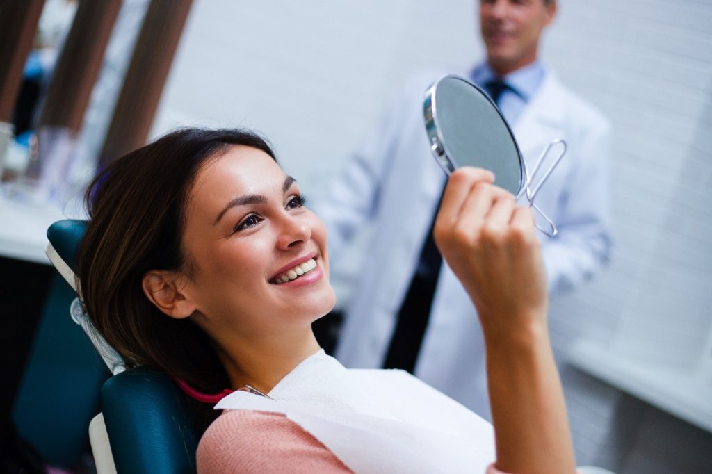 Patient with dental crowns looking at smile in dentist's mirror