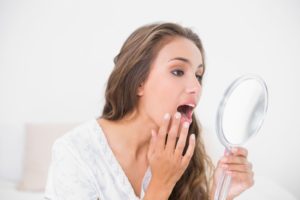 young woman looking at mouth in mirror
