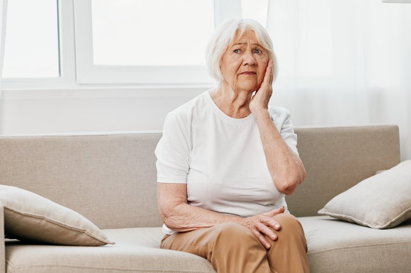 older woman sitting on couch with ill-fitting dentures